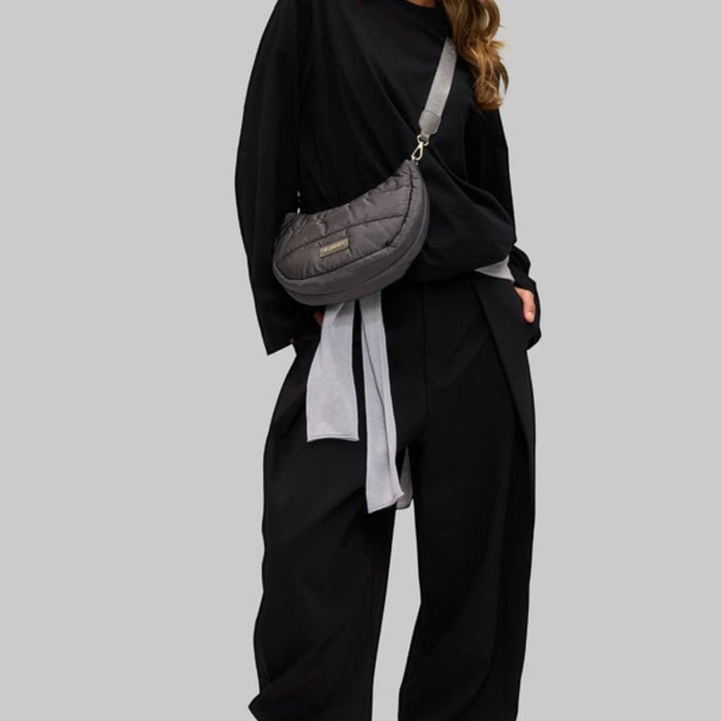 Model wearing a grey quilted Lieblingstasche Lifetime Buddy S crossbody bag with a wide adjustable strap
