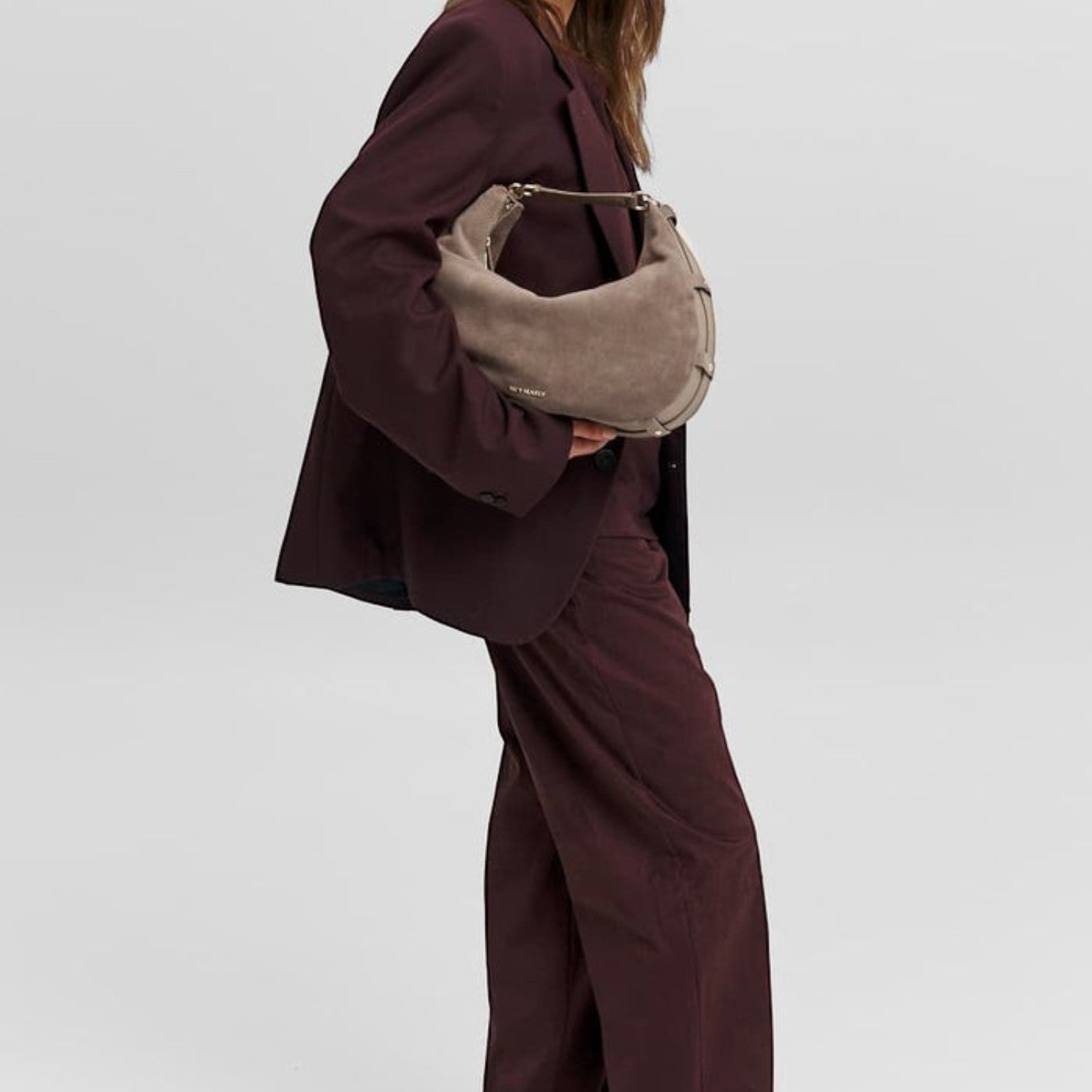 Lieblingstasche Lifetime Sister Suede M taupe suede hobo bag carried by a woman in a dark burgundy suit