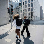 Two people walking in a city wearing Lieblingstasche Lisbon Pro black expandable travel backpacks with ergonomic straps.