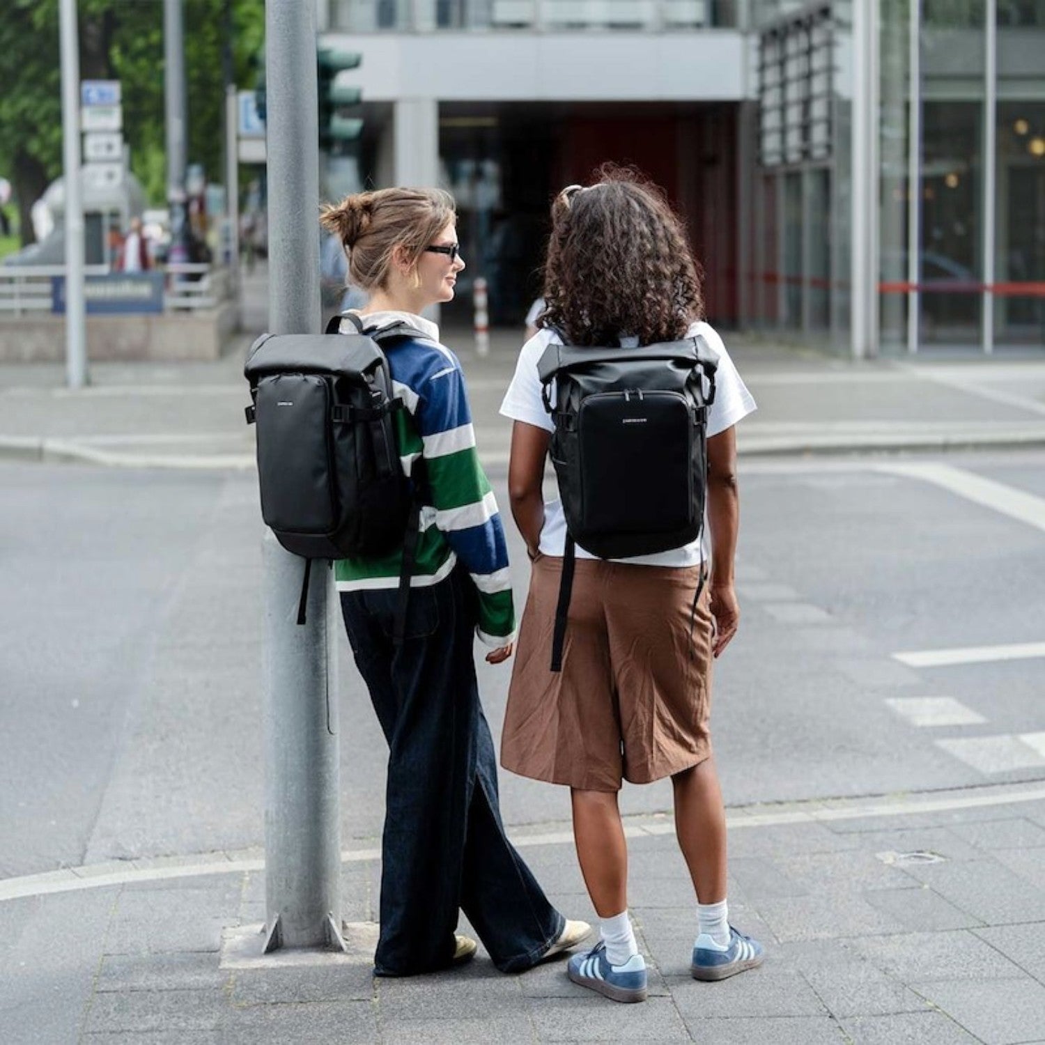 Two women wearing black Lieblingstasche Lisbon Small backpacks while standing on a city street.
