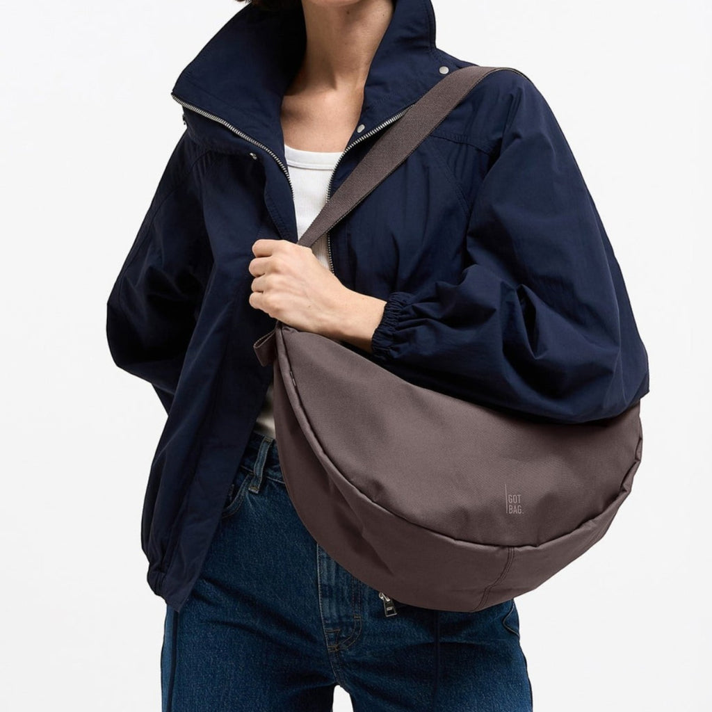 A woman wearing a Lieblingstasche Moon Bag Large in dark brown, styled as a crossbody bag with a casual jacket.