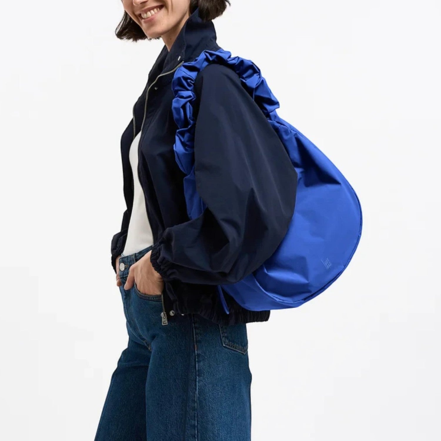 Lieblingstasche Moon Bag Ruffle Large in bright blue, worn as a shoulder bag by a smiling woman in a dark jacket.