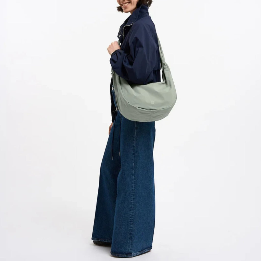 Lieblingstasche Moon Bag Ruffle Large in sage green, worn as a shoulder bag by a woman in a navy jacket and jeans.