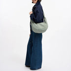 Lieblingstasche Moon Bag Ruffle Large in sage green, worn as a shoulder bag by a woman in a navy jacket and jeans.