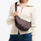 Lieblingstasche Moon Bag Small in dark brown worn as a crossbody bag by a woman in a cream zip-up sweater