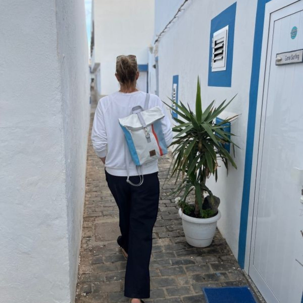 Lieblingstasche Möwe backpack with rolltop design in white, blue, and orange worn by a woman in a narrow alleyway.