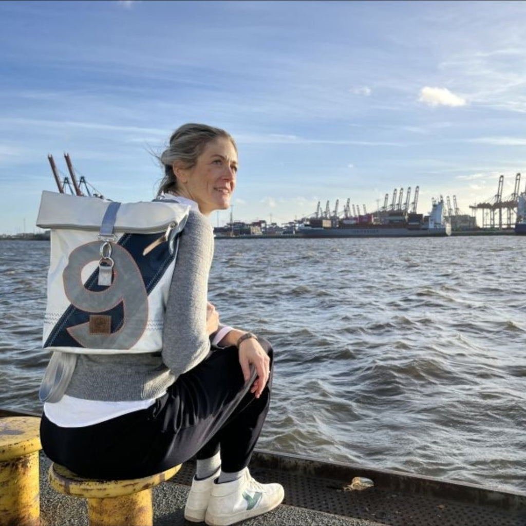 Lieblingstasche Möwe backpack with roll-top design and number 9 detail, worn by a woman sitting by the harbor.