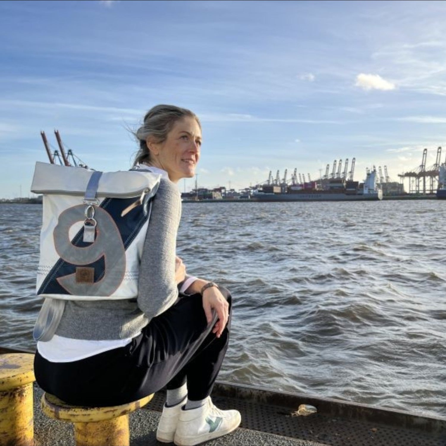Lieblingstasche Möwe backpack with roll-top design and number 9 detail, worn by a woman sitting by the harbor.