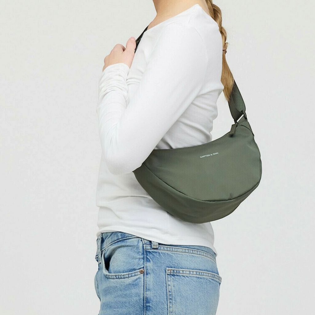 Lieblingstasche Essential Moon Bag in olive green worn over the shoulder by a woman in a white long-sleeve top
