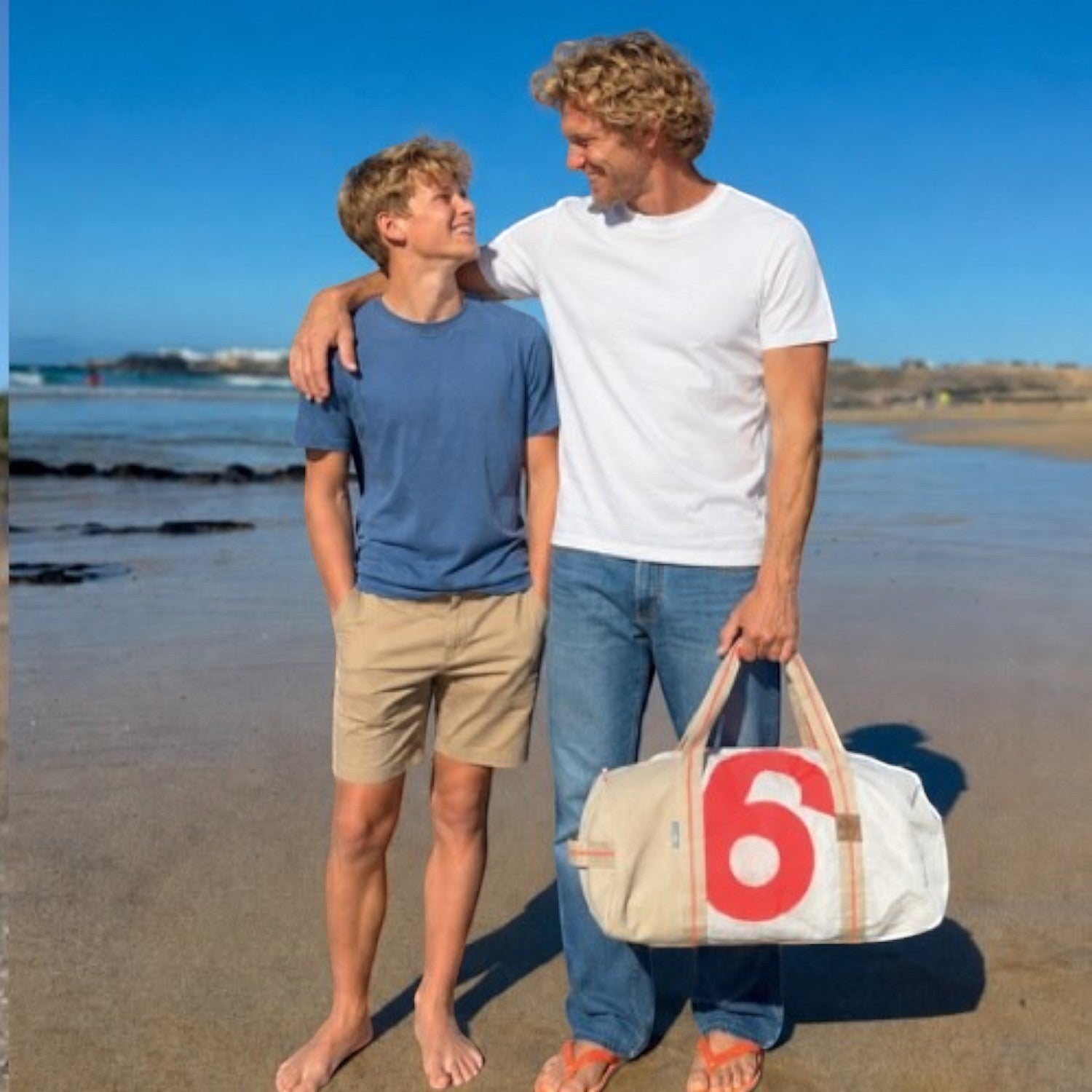 Lieblingstasche Pirat duffel bag with red number 6 print held by a man on a sunny beach with a teenager