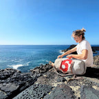 Woman sitting on a rocky cliff by the sea with a Lieblingstasche Pirat grey duffel bag featuring a red number six