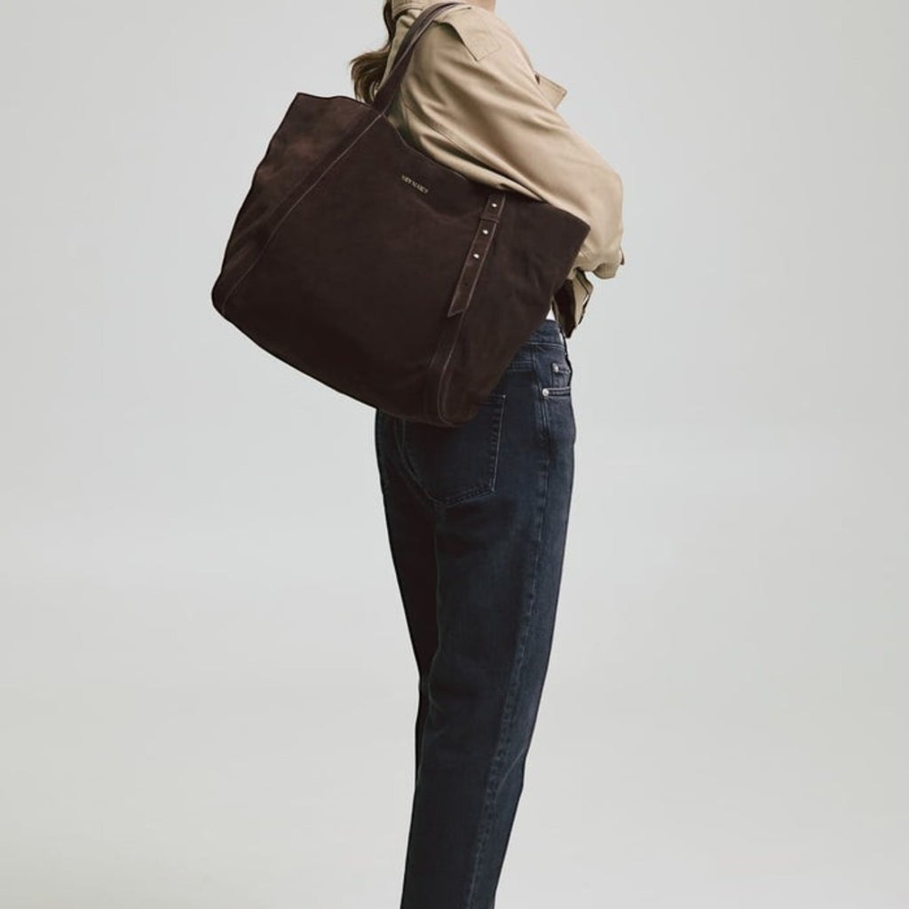 A woman carrying a dark brown suede Lieblingstasche Pretty Wonder Suede tote bag over her shoulder.