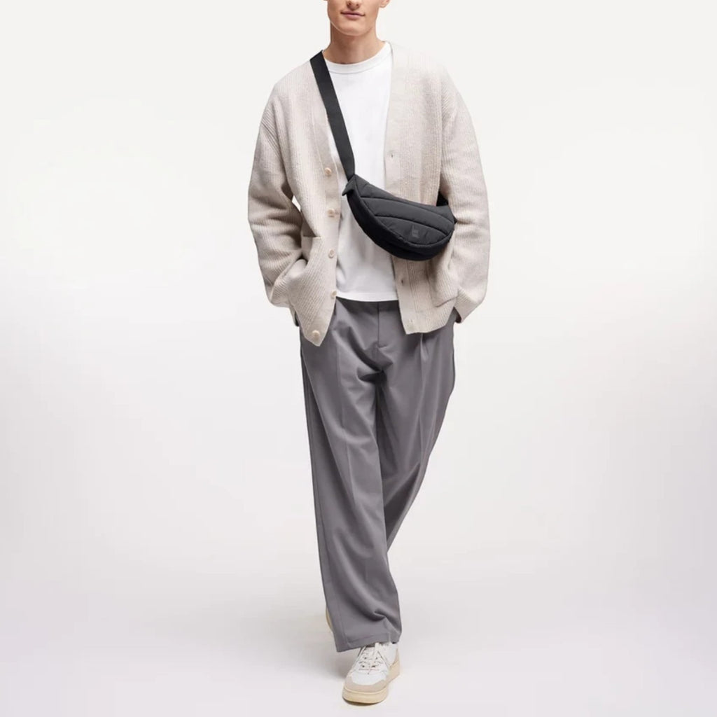 Lieblingstasche Puffer Moon Bag Small in black, worn crossbody by a model in a beige cardigan and grey trousers.