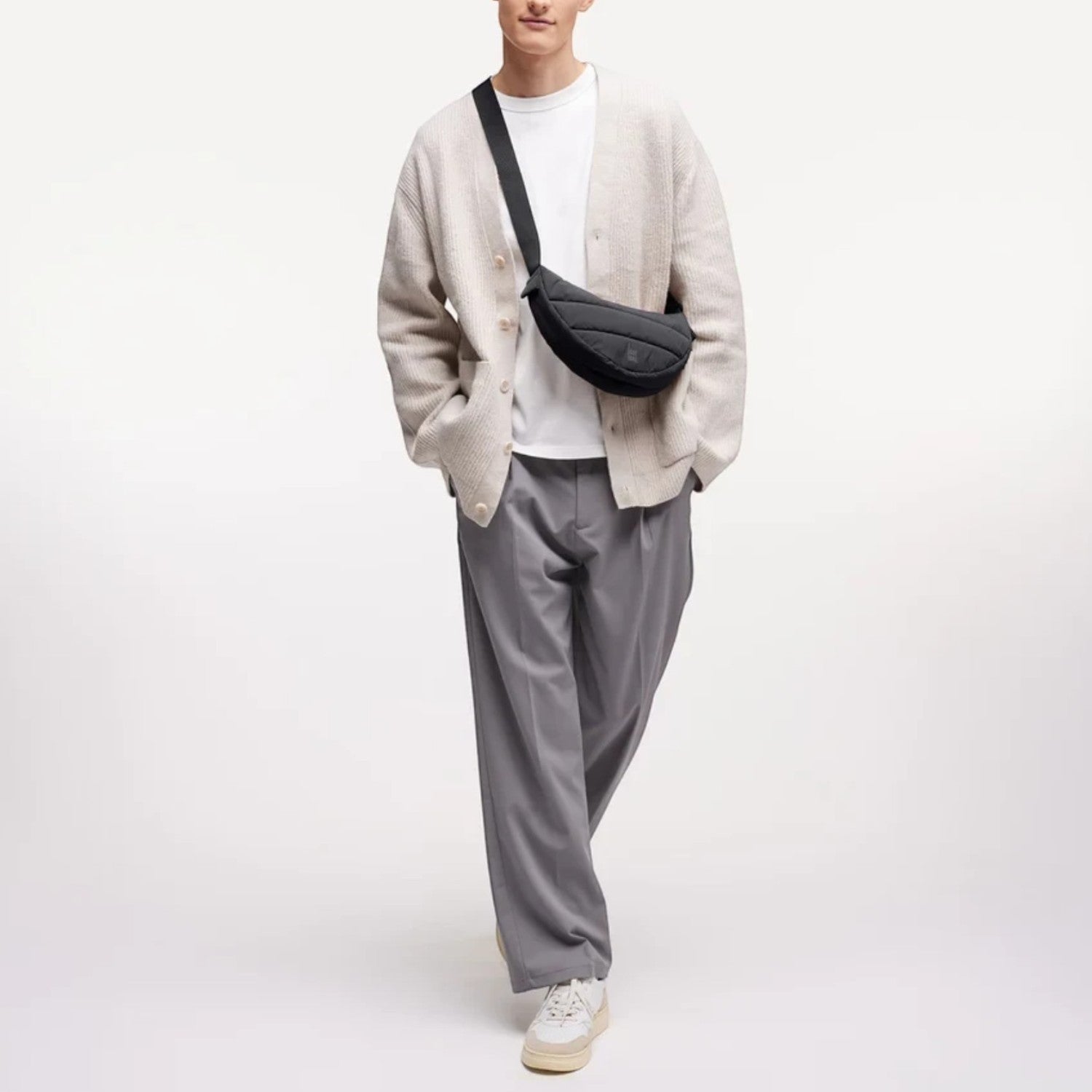 Lieblingstasche Puffer Moon Bag Small in black, worn crossbody by a model in a beige cardigan and grey trousers.