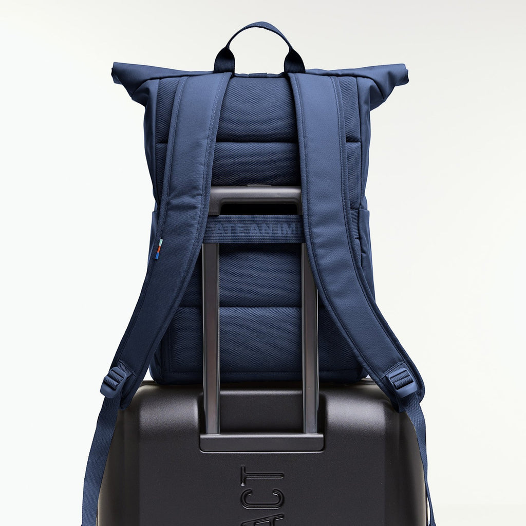 Lieblingstasche Rolltop Easy navy blue backpack with padded straps, attached to a black suitcase.