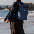 Lieblingstasche Rolltop Easy navy blue backpack with a roll-top closure and colorful zipper pull, worn by a person on a beach.