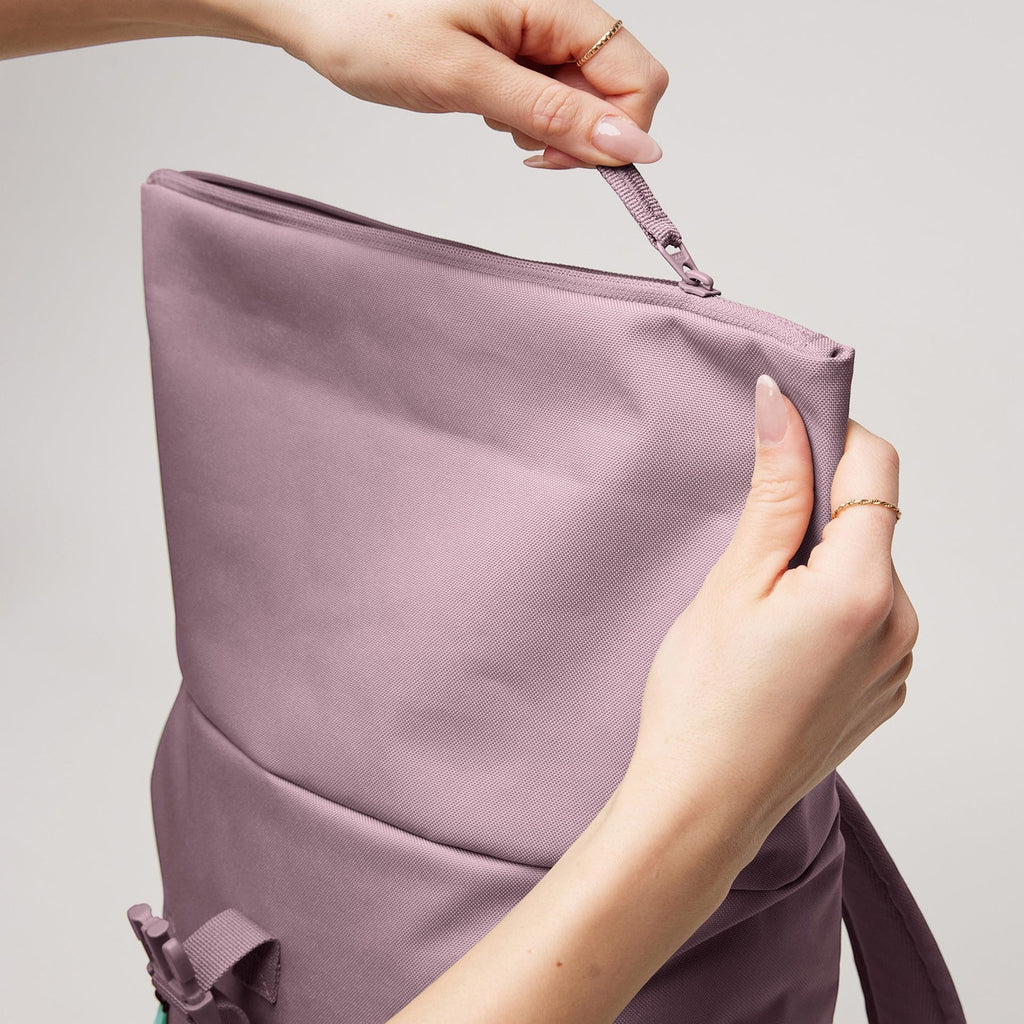 Lieblingstasche Rolltop Easy Small lilac canvas backpack being zipped closed by hands.