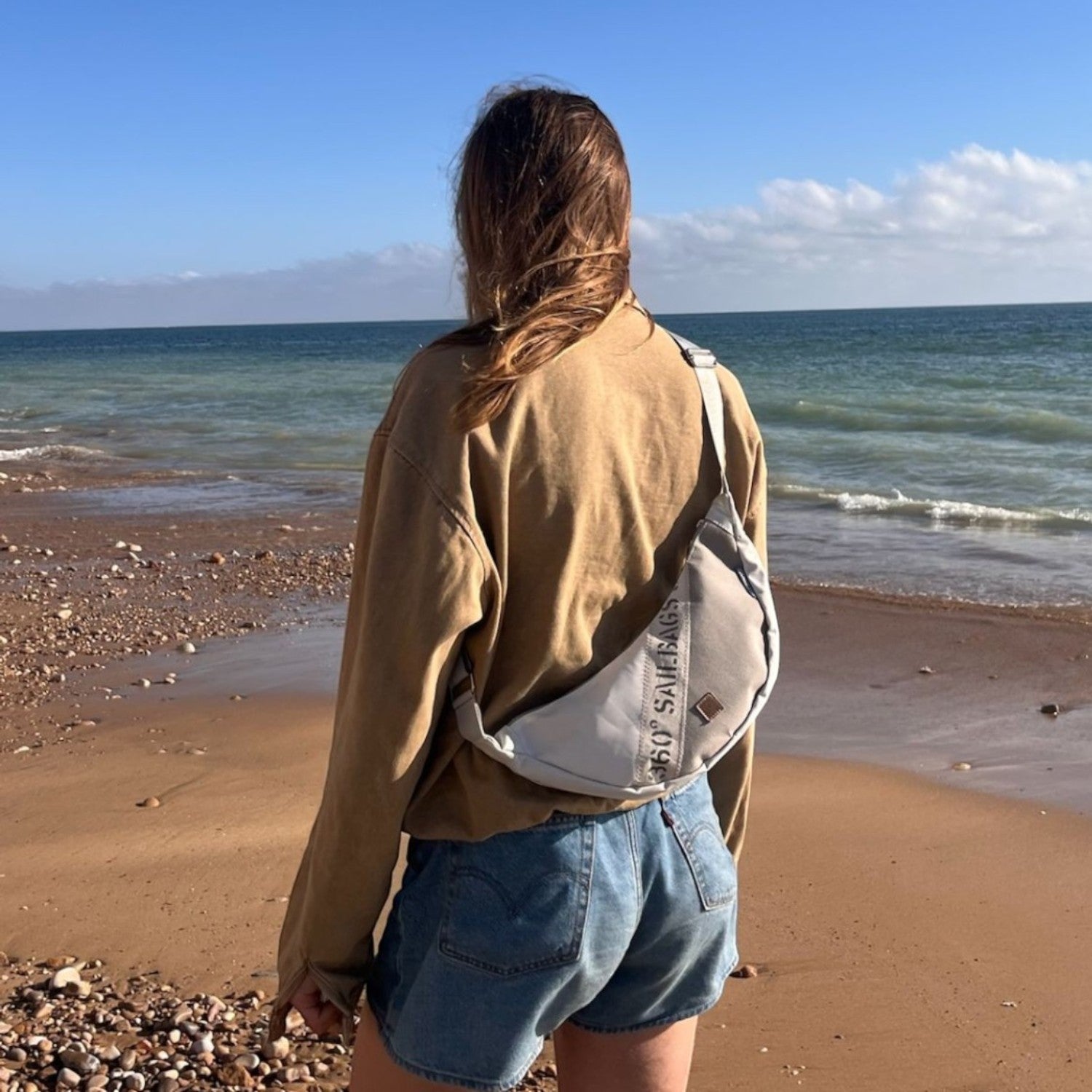 Lieblingstasche Roop moonbag made from recycled white sailcloth worn by a woman on a sunny beach