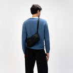 Man wearing a black Kapten & Son Skara Small crossbody bag from Lieblingstasche with a blue sweater and black jeans.