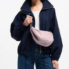 A woman wearing a Lieblingstasche small moon bag in dusty pink, styled as a crossbody bag over a navy jacket.