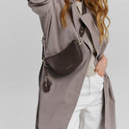 Lieblingstasche Sporty Sister dark brown leather crossbody bag worn by a blonde model in a grey trench coat