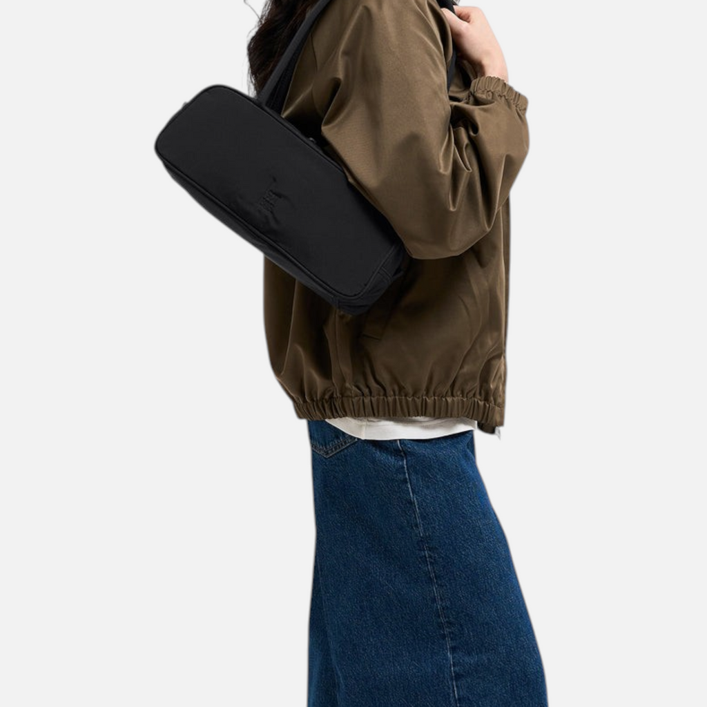 Lieblingstasche Strike Bag Small in black worn over the shoulder by a model in a brown jacket and blue jeans