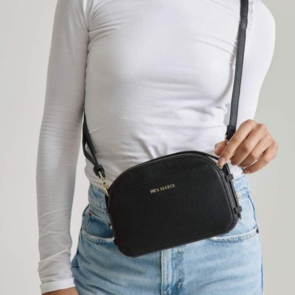 Lieblingstasche Style Mate black camera bag with gold hardware worn by a model in a white long-sleeve top