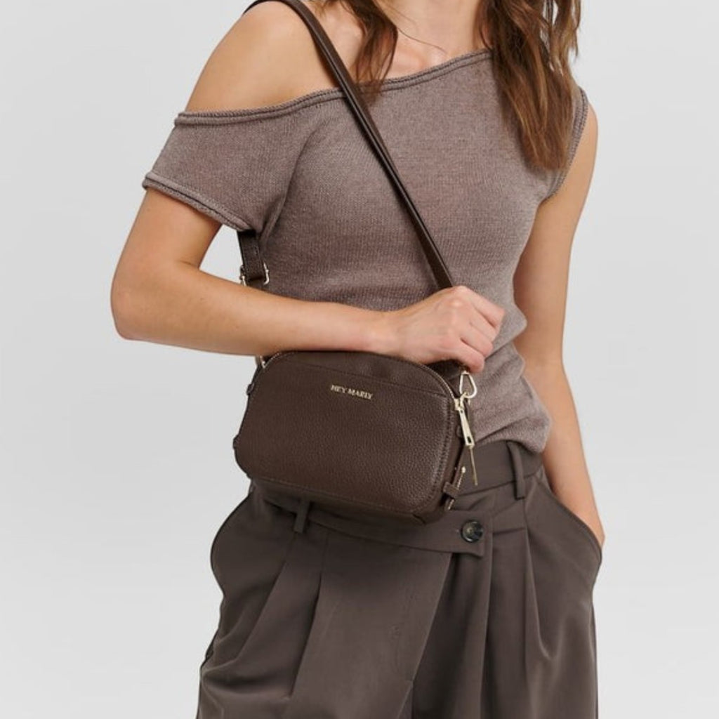 Woman wearing a dark brown Lieblingstasche Style Mate crossbody bag with gold hardware and a textured leather finish.