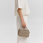 A woman wearing a cream-colored outfit holding a taupe Lieblingstasche Style Mate crossbody bag.
