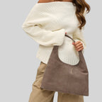 A woman wearing a white ribbed sweater holding a taupe Lieblingstasche Alltime Lover ReSuede M shoulder bag