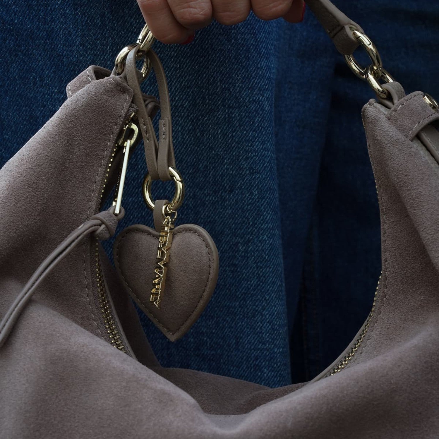 Lieblingstasche heart charm in taupe suede hanging from a matching handbag with gold hardware