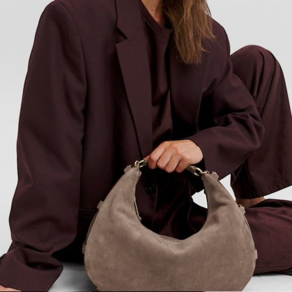 Lieblingstasche Lifetime Sister suede hobo bag in taupe held by a model wearing a matching dark burgundy suit