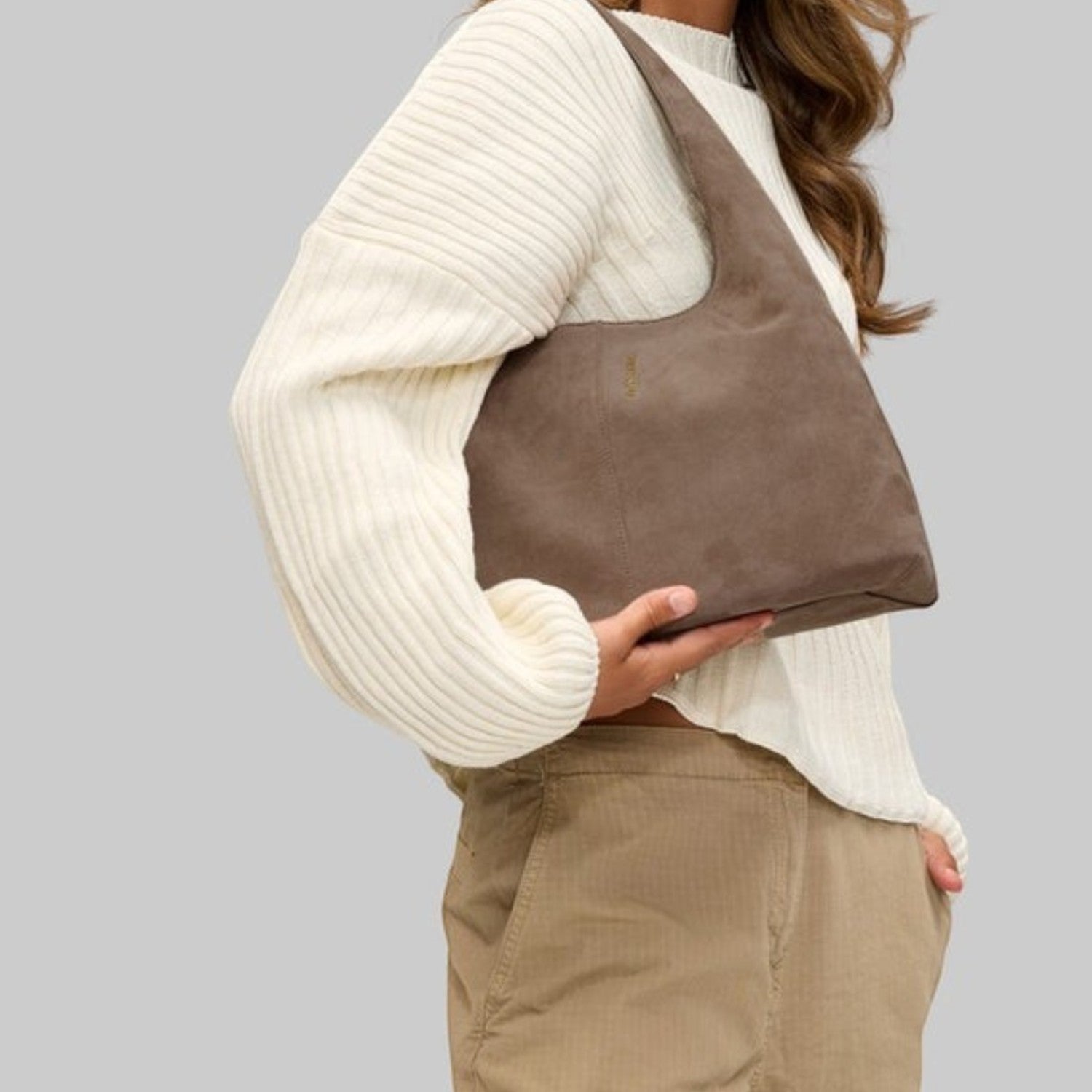 Woman wearing a Lieblingstasche Alltime Lover ReSuede M shoulder bag in taupe suede, styled with a cream sweater.