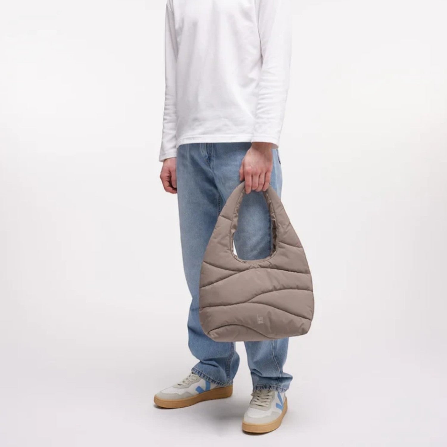 Lieblingstasche wavy puffer shoulder bag in taupe held by a smiling man wearing a white long-sleeve shirt and jeans.