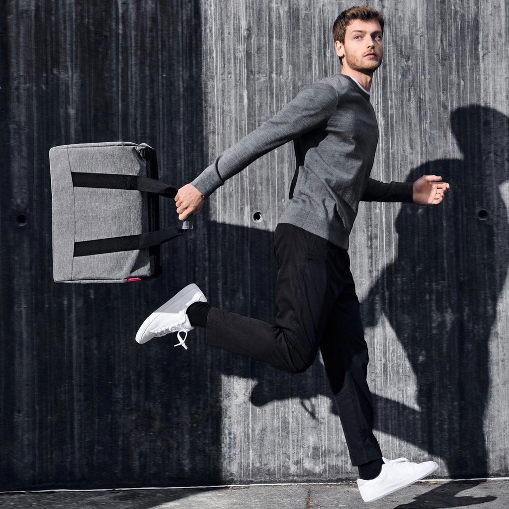 Lieblingstasche Allrounder L grey travel bag held by a man in a grey sweater running against a concrete wall